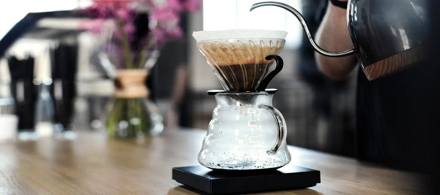 Coffee brewing process with a glass carafe and filter on a wooden table.