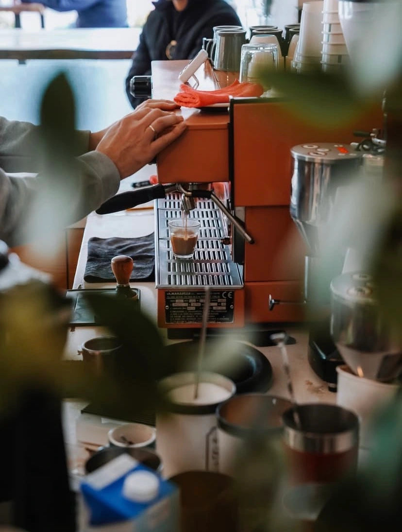 Person making coffee using a manual espresso machine in a cafe setting.